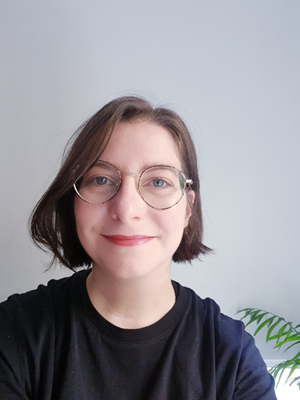 Photo professionnelle Sophie Hellégouarch. Portrait sur fond blanc, elle porte un t-shirt noir, des lunettes, cheveux chatain, en carré.